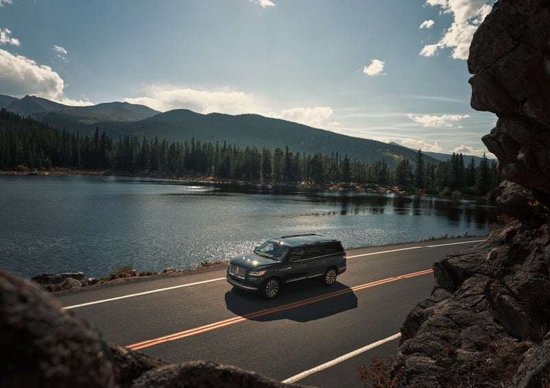 A 2022 Lincoln Navigator SUV is driving along a lake high up in the mountains | Klaben Lincoln in Kent OH