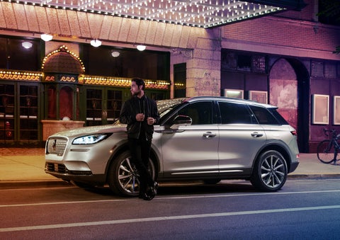 A 2022 Lincoln Corsair SUV is parked outside a theater as the driver relaxes against the frame and lights illuminate the floating roofline and body | Klaben Lincoln in Kent OH