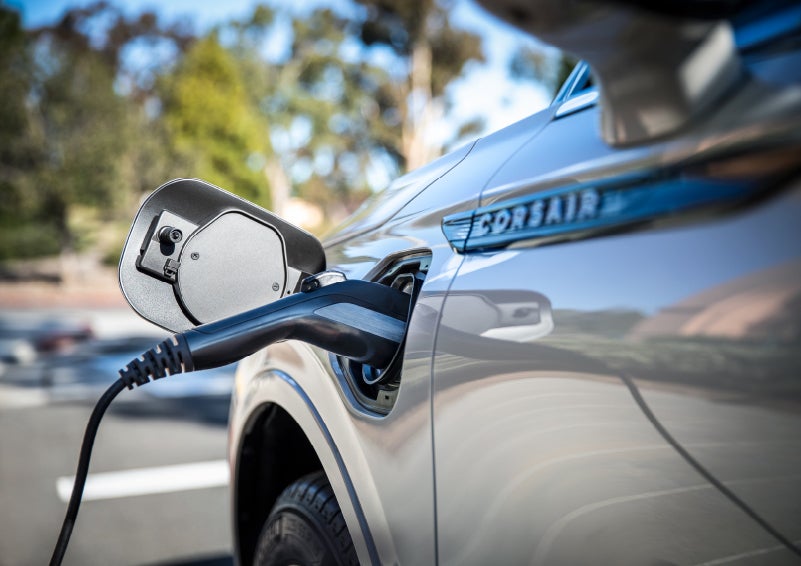 A Lincoln electric charger is plugged into a 2022 Lincoln Corsair Grand Touring port as the body reflects the surroundings of a sun-soaked parking lot | Klaben Lincoln in Kent OH