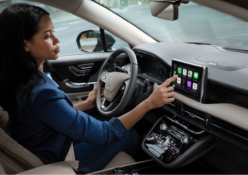 A woman in the driver’s seat of a 2022 Lincoln Corsair is touching the center digital screen to connect to Apple CarPlay<sup>®</sup> | Klaben Lincoln in Kent OH