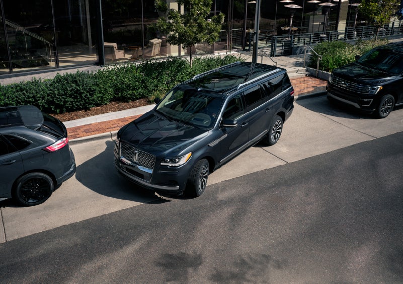 A 2022 Lincoln Navigator SUV is being parallel parked between two vehicles on a downtown street outside of a luxury hotel | Klaben Lincoln in Kent OH