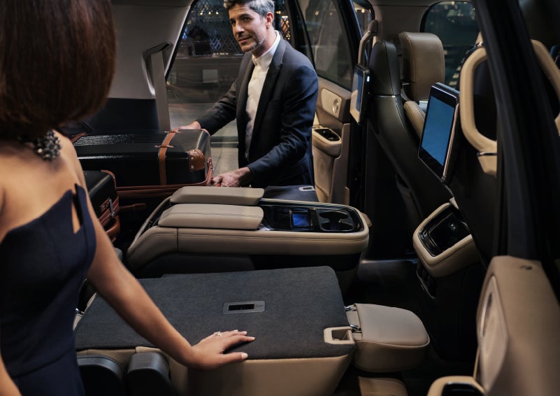 A man is pulling a suitcase out of the folded flat second-row of a 2022 Lincoln Navigator SUV | Klaben Lincoln in Kent OH