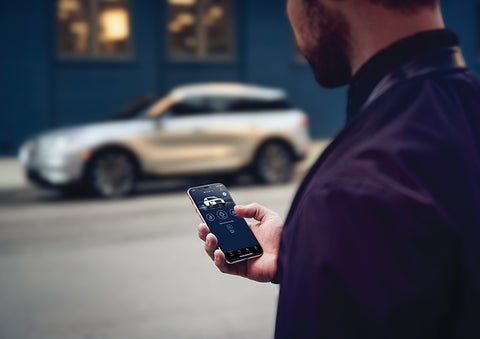 A person is shown interacting with a smartphone to connect to a Lincoln vehicle across the street. | Klaben Lincoln in Kent OH