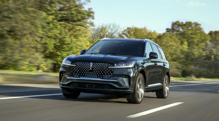 A 2025 Lincoln Black Label Aviator® SUV is being driven down a road lined with trees. | Klaben Lincoln in Kent OH