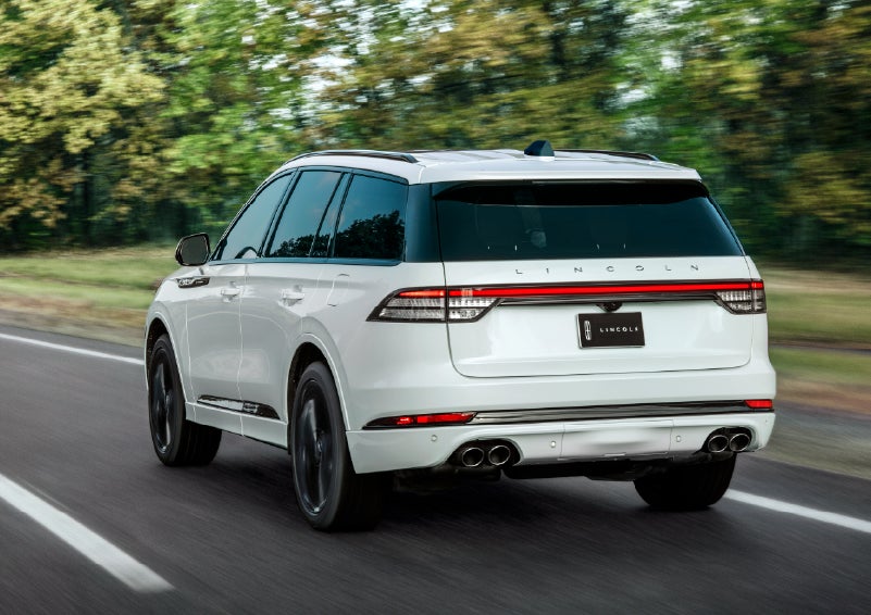 A white 2026 Lincoln Aviator® SUV is being driven away down a road lined with colorful trees. | Klaben Lincoln in Kent OH