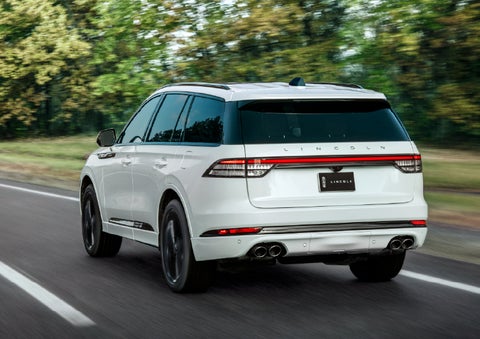 A white 2026 Lincoln Aviator® SUV is being driven away down a road lined with colorful trees. | Klaben Lincoln in Kent OH