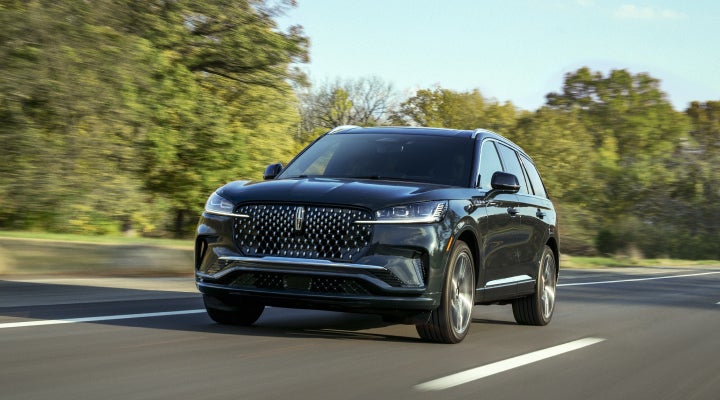A 2026 Lincoln Black Label™ Aviator® SUV is being driven down a road lined with trees. | Klaben Lincoln in Kent OH