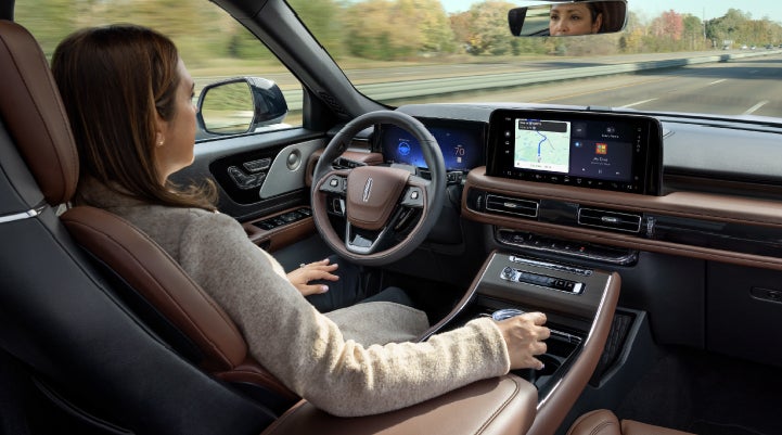 A 2027 Lincoln Aviator® SUV is being driven hands-free on a highway lined with trees. | Klaben Lincoln in Kent OH