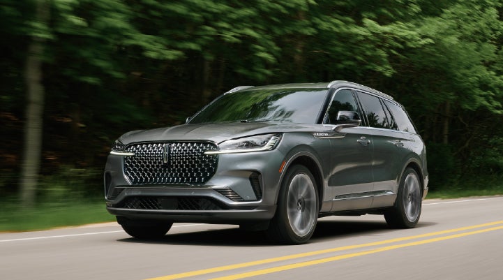 A 2027 Lincoln Aviator® SUV is being driven down a road lined with trees. | Klaben Lincoln in Kent OH
